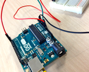 Photo d'une petite carte électronique Arduino avec ses composants : processeur, prise réseau, connecteurs avec fils électriques branchés.