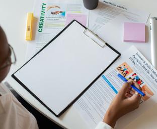 Image décorative représentant une jeune femme noire assise à une table devant des documents éparpillés.