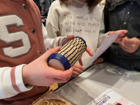 Photo d’un enfant essayant d’ouvrir un coffre cylindrique en bois, appelé "cryptex"