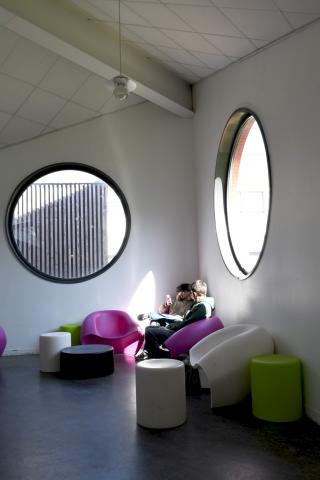 Espace libre du Ty-Maz', muni de deux fenêtres en forme de hublots, où deux étudiants sont en train de discuter dans des fauteuils