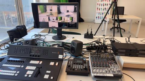 Photo du studio audiovisuel représentant au premier plan un écran d'ordinateur, des enceintes et trois tables de mixage. En arrière-plan, une caméra sur pied.
